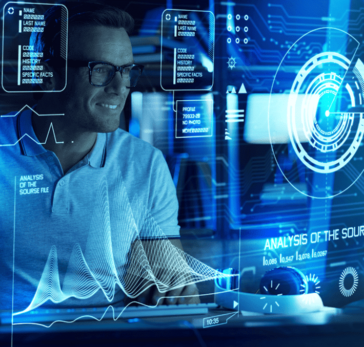 Person in glasses works on a computer with futuristic digital interfaces displaying data analysis and graphs.