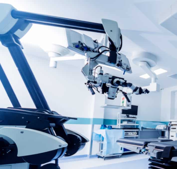 Robotic surgical equipment, expertly crafted by biomedical and clinical engineers, stands in a modern operating room with bright lighting and various medical devices.