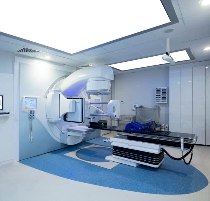 A cutting-edge medical radiation therapy room features a large linear accelerator machine, blue flooring, and overhead lighting, showcasing innovation similar to replacing Excel with a product configurator.