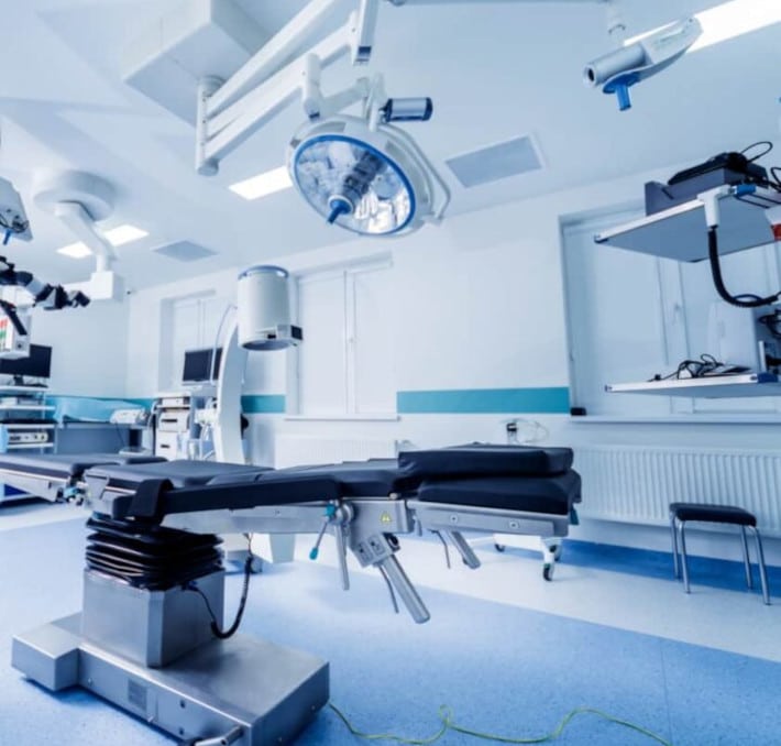 A modern medical equipment planning operating room showcases expertly installed medical equipment, featuring surgical tools and overhead lights. The space is defined by blue and white walls and floors, with various machines and monitors seamlessly integrated for optimal care.