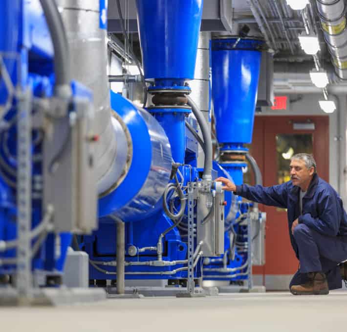 A person in a blue uniform inspects large blue industrial machinery in a facility, uncovering the secrets of how fluid processing systems work efficiently.