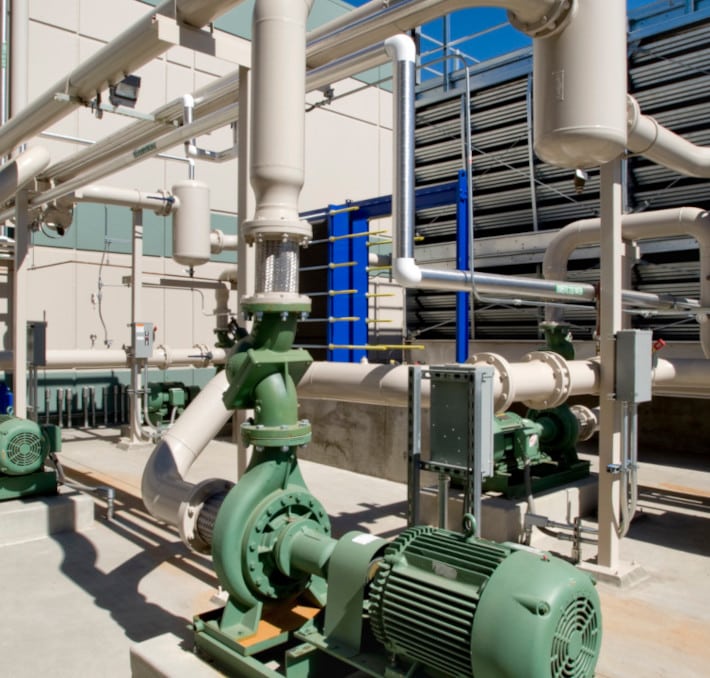 An industrial setup features interconnected piping and green machinery, enhanced by a digital twin for fluid management. Valves punctuate the scene, all set against a backdrop of a blue sky and towering building.
