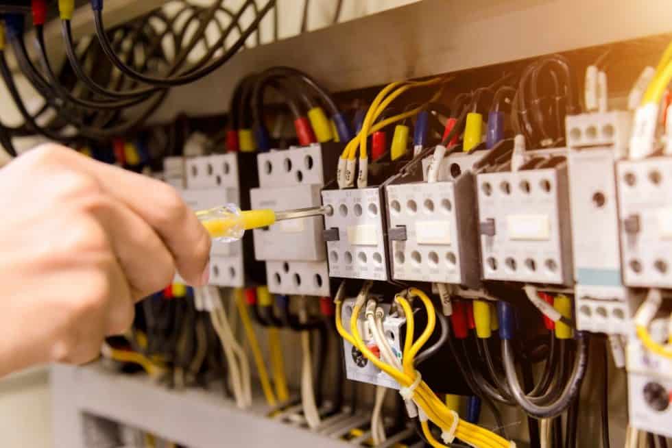 A hand deftly uses a screwdriver on an electrical panel adorned with various wires and switches, showcasing the technical proficiency essential in the diverse industries eRep serves.