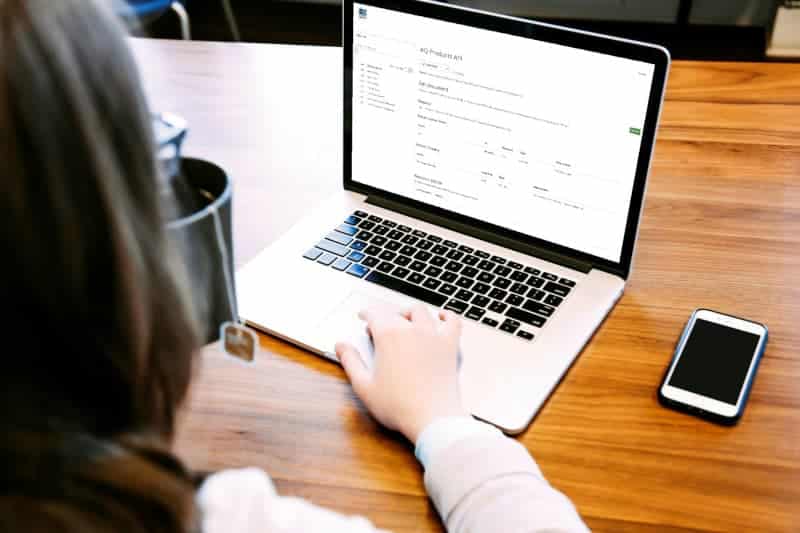 A person is using a laptop with a document open on the screen, integrating AQ API seamlessly into their workflow. They sit at a wooden desk with a smartphone beside them, focused and efficient.