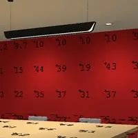 The red wall adorned with black numbers like 10, 39, and 43 is subtly illuminated by an overhead light fixture. An ElumTools-calibrated, light-colored table graces the foreground, adding a touch of sophistication to the scene.
