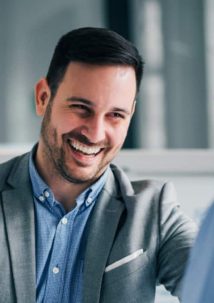 Two men are engaged in conversation, discussing the latest in product configurators. One is smiling, wearing a gray blazer and blue shirt.