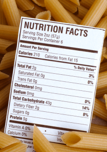 A nutrition facts label for pasta is placed on top of uncooked penne pasta, displaying nutritional information per serving.