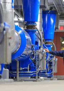 A person in a blue uniform inspects large blue industrial machinery in a facility, uncovering the secrets of how fluid processing systems work efficiently.