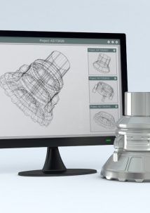 A computer monitor displays a 3D wireframe model of a mechanical part, with the corresponding real-world metal component placed beside it.